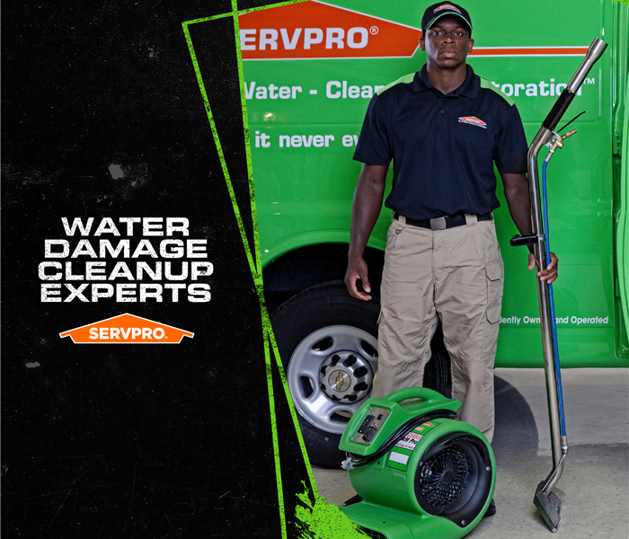 A SERVPRO tech standing in front of a SERVPRO truck holding water clean up tools.
