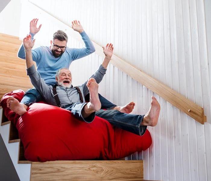 Two men sliding down a set of stairs on a big red pillow. 
